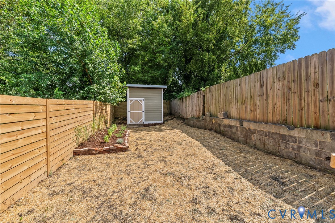 Outdoor area featuring horizontal wood fencing, a masonry retaining wall, a detached storage shed, and a raised garden bed with brick edging