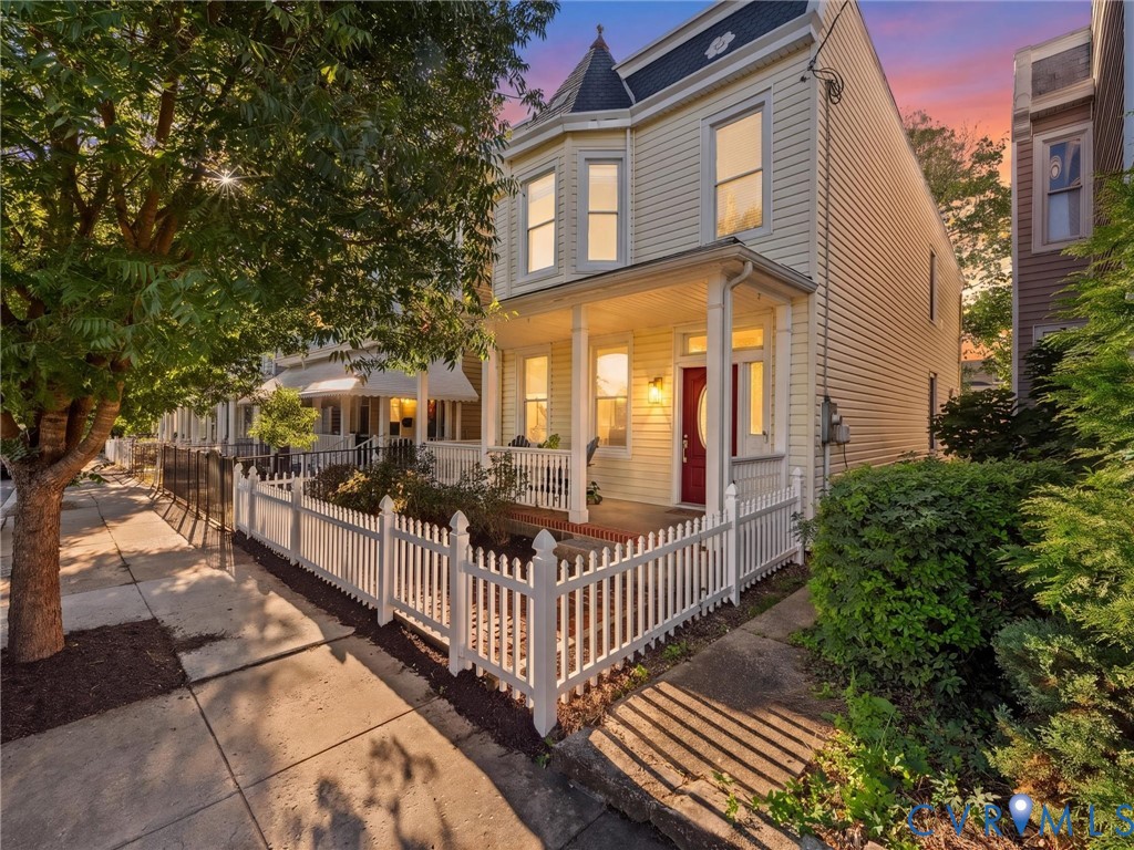 Victorian-inspired exterior featuring light-toned siding, a covered front porch, a turret, and a white picket fence
