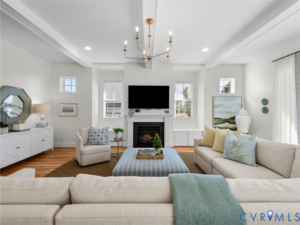Living area featuring high ceilings with exposed beams, wood-finish flooring, a central fireplace with a classic mantel, built-in cabinetry, and a modern chandelier