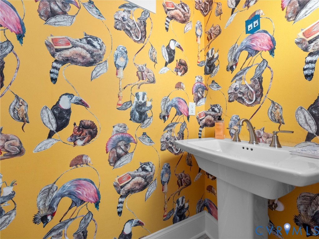 Pedestal sink with a polished metal dual-handle faucet, accented by bold, illustrative botanical and wildlife wallpaper