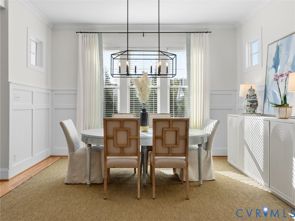 Dining space featuring white wainscoting, a black iron rectangular chandelier, triple window configuration, and white built-in cabinetry with arched detailing