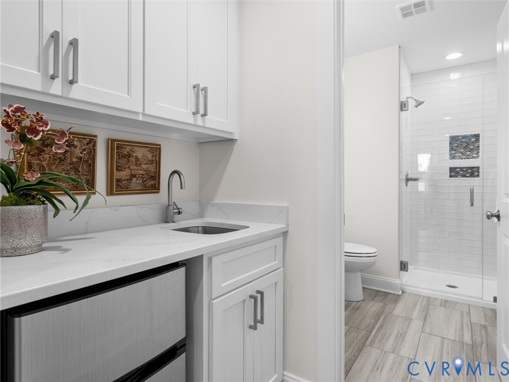 White shaker-style cabinetry with satin nickel hardware, stone-composite countertop, stainless steel undermount sink, and tiled walk-in shower featuring a mosaic-tile recessed niche