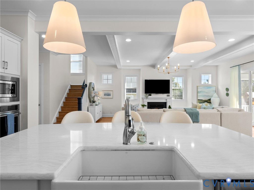 Kitchen island featuring a white stone countertop, undermount farmhouse sink, and high-arc faucet, complemented by oversized pendant lighting and coffered ceilings