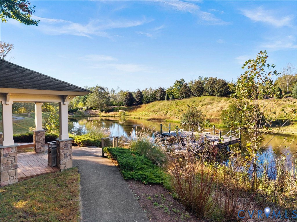 Covered pavilion featuring stone-base columns and wood decking, paved walkway, private pond, and timber-frame dock with rope railings