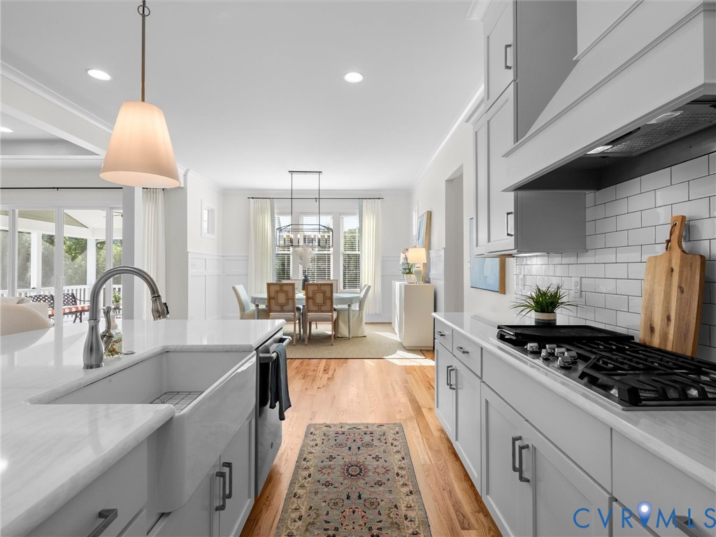 Kitchen featuring a white farmhouse sink, light-toned quartz countertops, subway tile backsplash, ceiling-height cabinetry, and wood-finish flooring