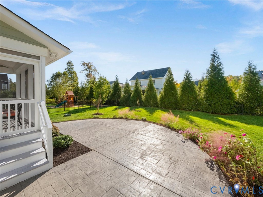 Backyard featuring a stamped concrete patio, screened porch, perimeter metal fencing, and mature evergreen privacy screening