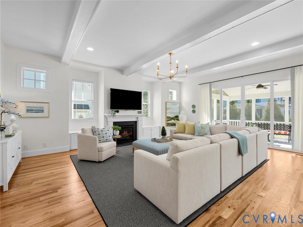 Open-concept living space featuring wood-finish flooring, vaulted ceilings with exposed beams, a fireplace with a mantel, and large sliding glass doors providing access to a screened porch