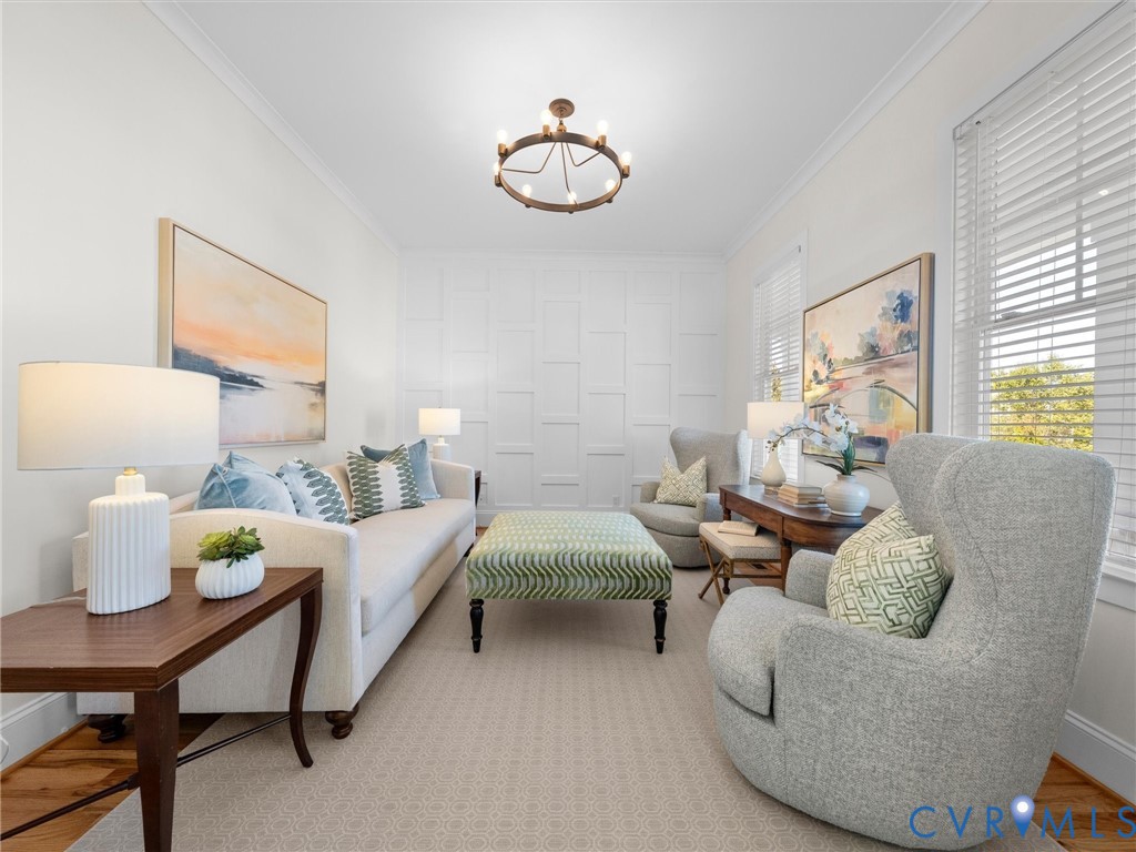 Living area featuring white paneled accent wall, crown molding, circular chandelier, and horizontal window blinds