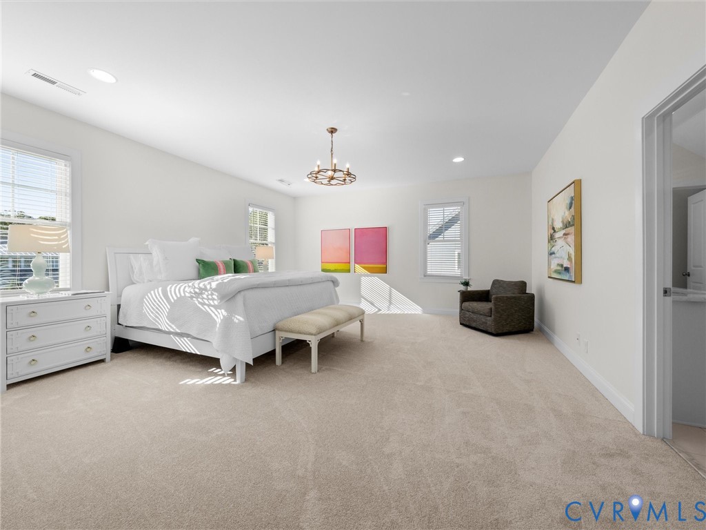Spacious room featuring neutral carpeting, multi-pane windows, recessed lighting, and a tiered metal chandelier