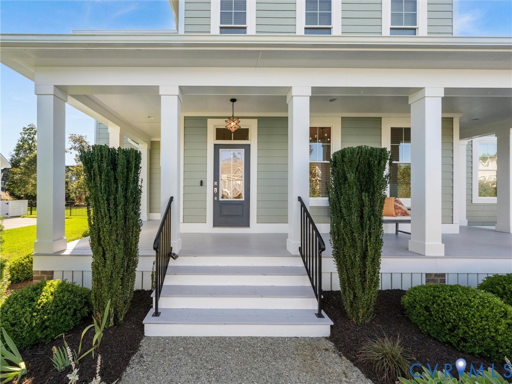 Covered front porch featuring white square columns, light green horizontal siding, multi-pane glass entry door, and black metal handrails Covered front porch featuring white square columns, light green horizontal siding, multi-pane glass entry door, and black metal handrails