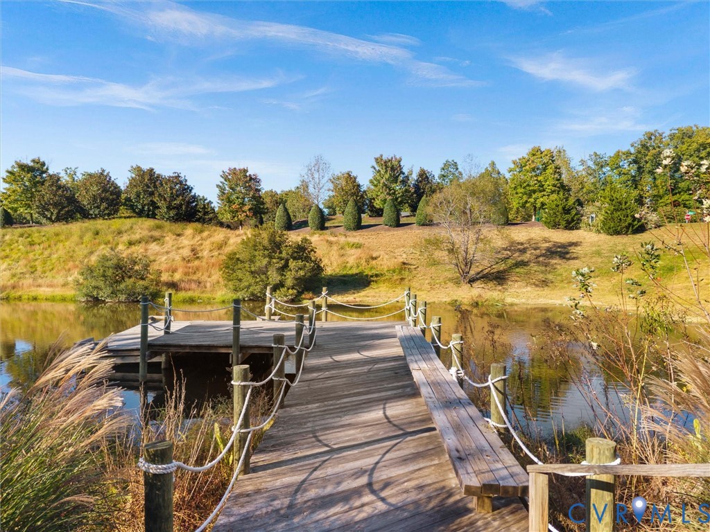 Wooden dock featuring integrated bench seating and rope-style handrails extending over a private pond with landscaped shoreline