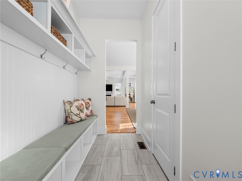 Mudroom featuring built-in cabinetry with beadboard detailing, open cubby storage, integrated bench seating, and wood-finish flooring in the adjoining space