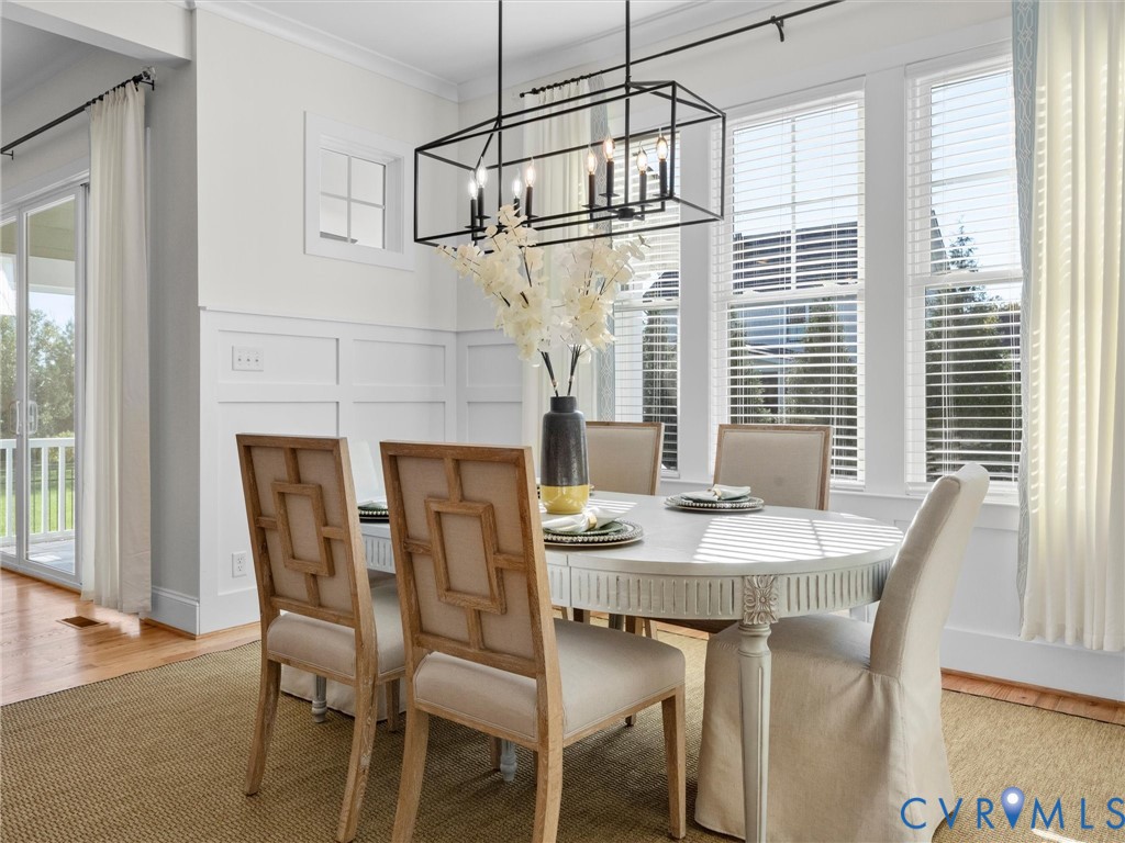 Dining area featuring wainscoting, an open-frame matte black chandelier, and multiple windows with horizontal blinds