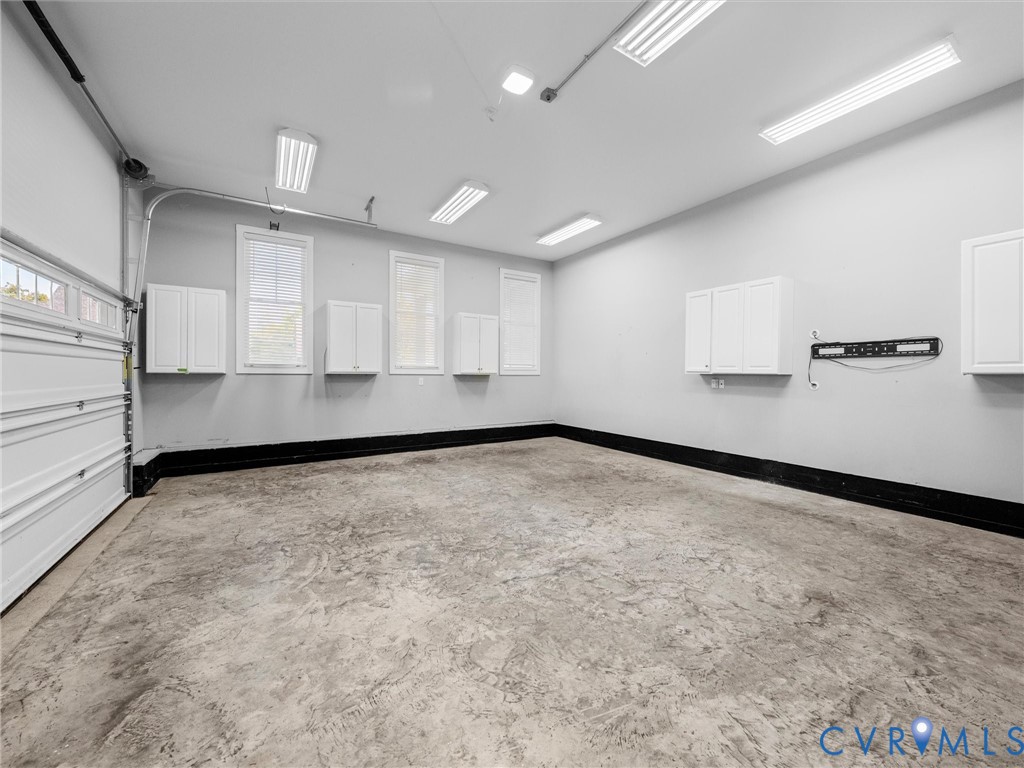 Spacious garage featuring a concrete floor, built-in white cabinetry, multiple windows, and overhead fluorescent lighting