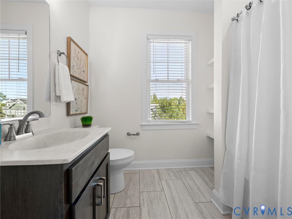 Bathroom featuring a dark wood-finish vanity with a stone-top integrated sink, ceramic tile flooring, a shower-tub combination, and built-in wall shelving
