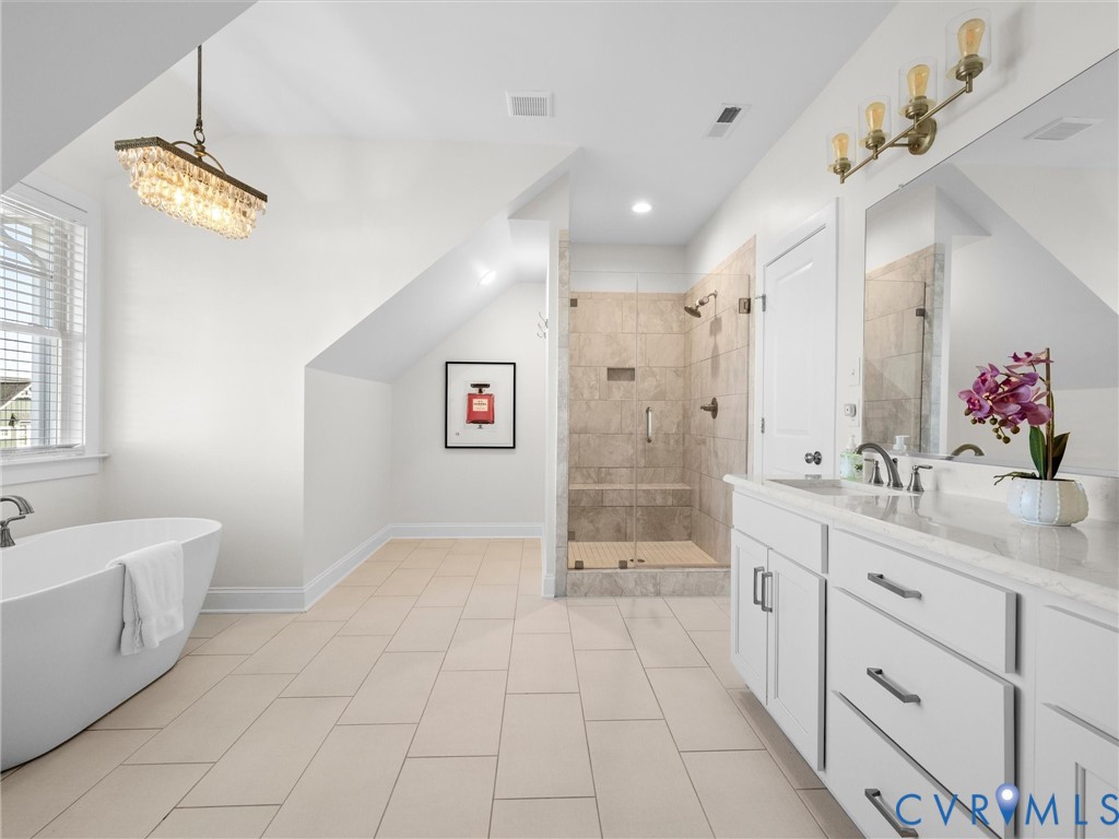 Freestanding soaking tub, walk-in shower with tile surround and built-in bench, dual-sink vanity with light-colored stone countertop, and glass-front lighting fixtures