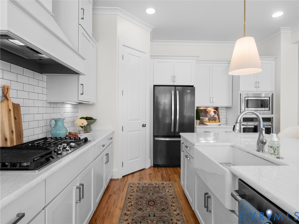 Kitchen featuring white cabinetry, subway tile backsplash, farmhouse-style apron sink, stone countertops, and stainless steel appliances
