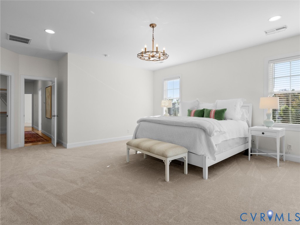 Spacious room featuring neutral carpeting, recessed lighting, a multi-arm chandelier, and large windows with integrated blinds