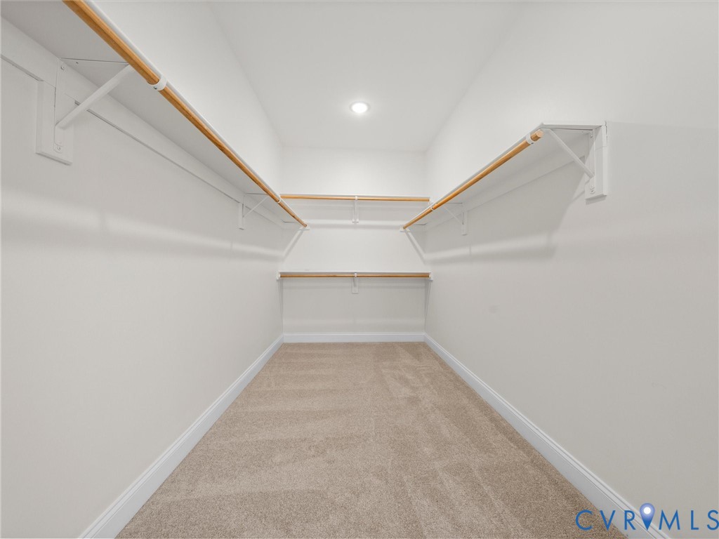 Walk-in closet featuring tiered shelving with wood-finish rods, neutral wall-to-wall carpeting, and recessed lighting