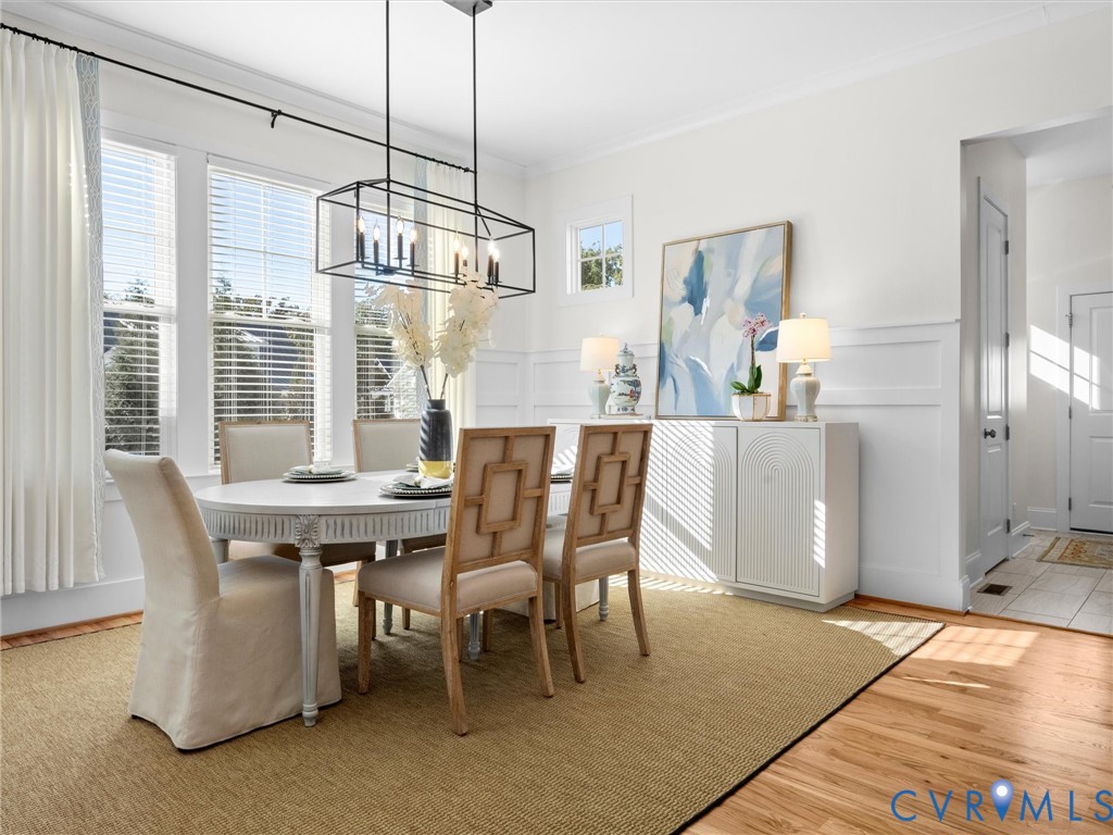 Dining area featuring wood-finish flooring, white wall wainscoting, multi-pane windows, and a rectangular metal-frame pendant light fixture