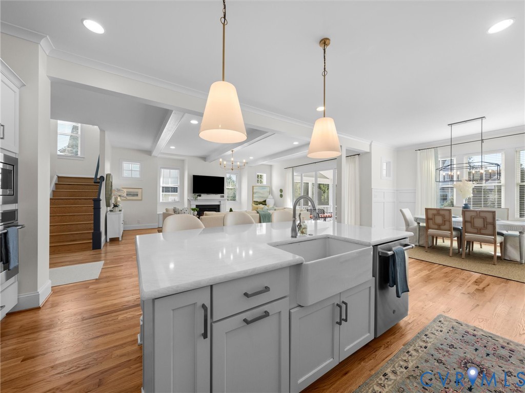 Kitchen island featuring a farmhouse sink, quartz countertop, and matte hardware, complemented by wood-finish flooring and dual pendant lighting