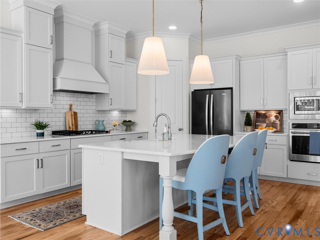 Kitchen featuring white cabinetry, center island with stone countertop, subway tile backsplash, stainless steel built-in appliances, and wood-finish flooring