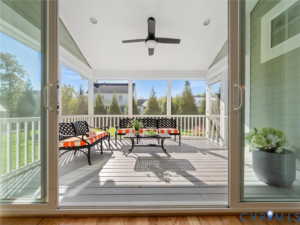 Screened porch featuring painted wood decking, a vaulted ceiling, a matte black ceiling fan, and white railing