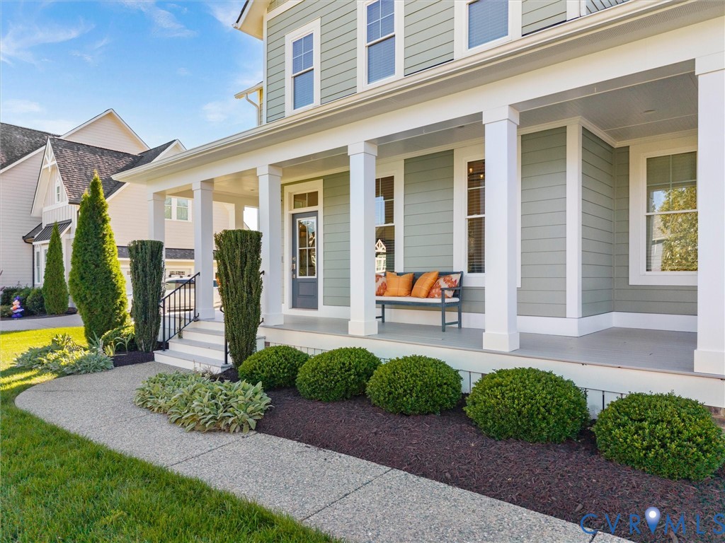 Covered front porch featuring white square columns, lap siding, a glass-paneled entry door, and a concrete walkway Covered front porch featuring white square columns, lap siding, a glass-paneled entry door, and a concrete walkway