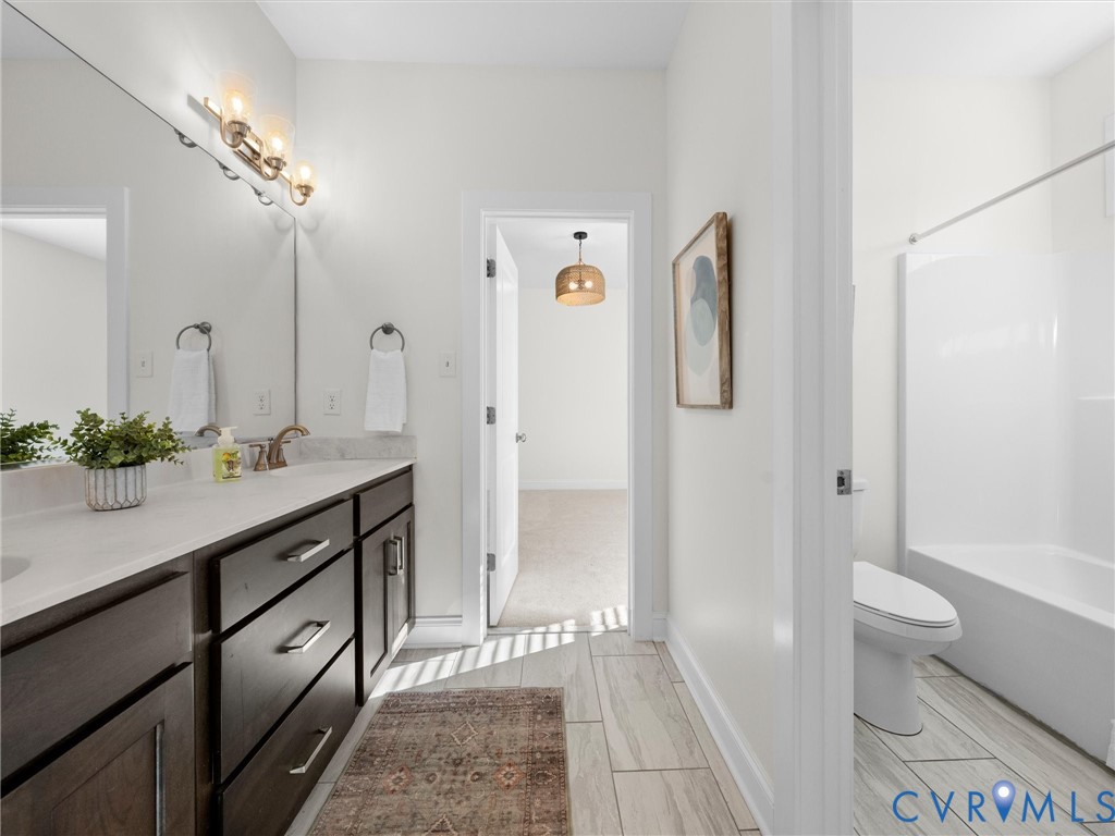 Dark wood cabinetry with metallic hardware, stone countertop, integrated vanity sink, polished lighting fixtures, and tile flooring