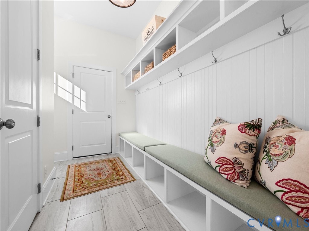 Built-in storage bench featuring white millwork, beadboard paneling, open cubbies, and metal coat hooks, finished with wood-finish tile flooring