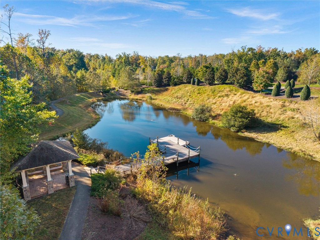 Private pond featuring a stone-based gazebo, wood-plank pier with rope railings, paved pathways, and mature landscaping