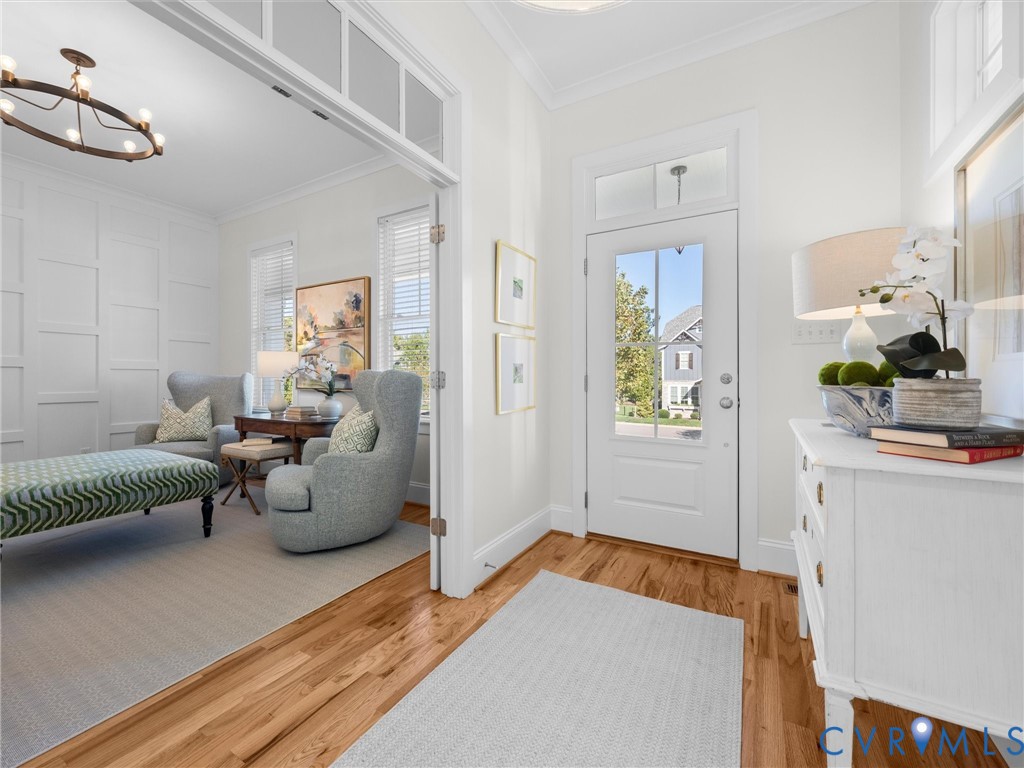 Foyer featuring wood-finish flooring, a glass-panel entry door with transom window, and white wainscoting wall paneling Foyer featuring wood-finish flooring, a glass-panel entry door with transom window, and white wainscoting wall paneling