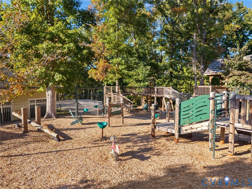 Backyard playground featuring a wooden multi-level climbing structure, slide, teeter-totter, and fenced pool area surrounded by mature trees