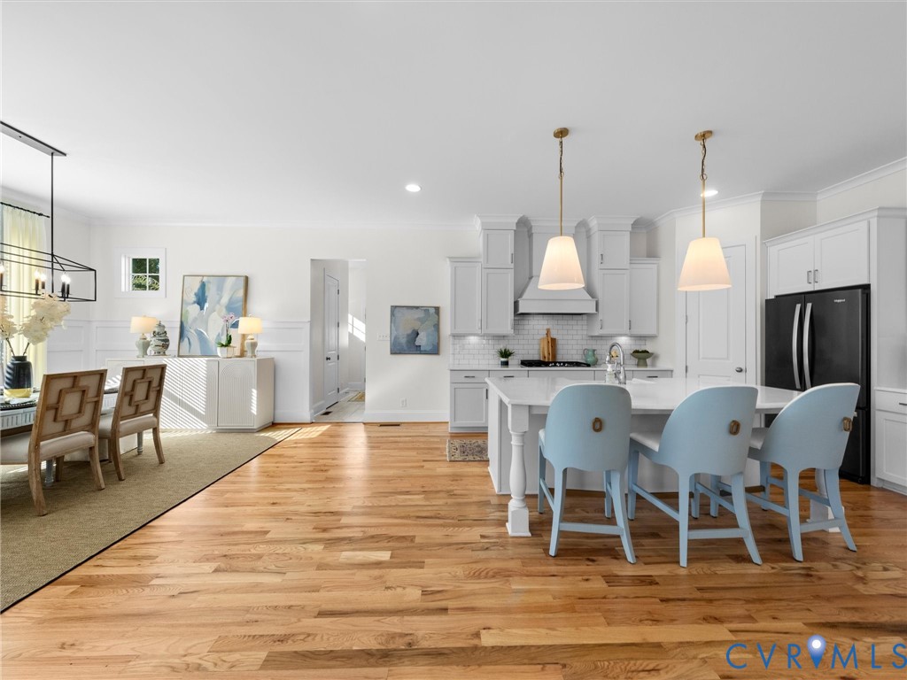 Open kitchen and dining area featuring wood-finish flooring, white shaker-style cabinetry, a stone-topped island with seating, and pendant lighting