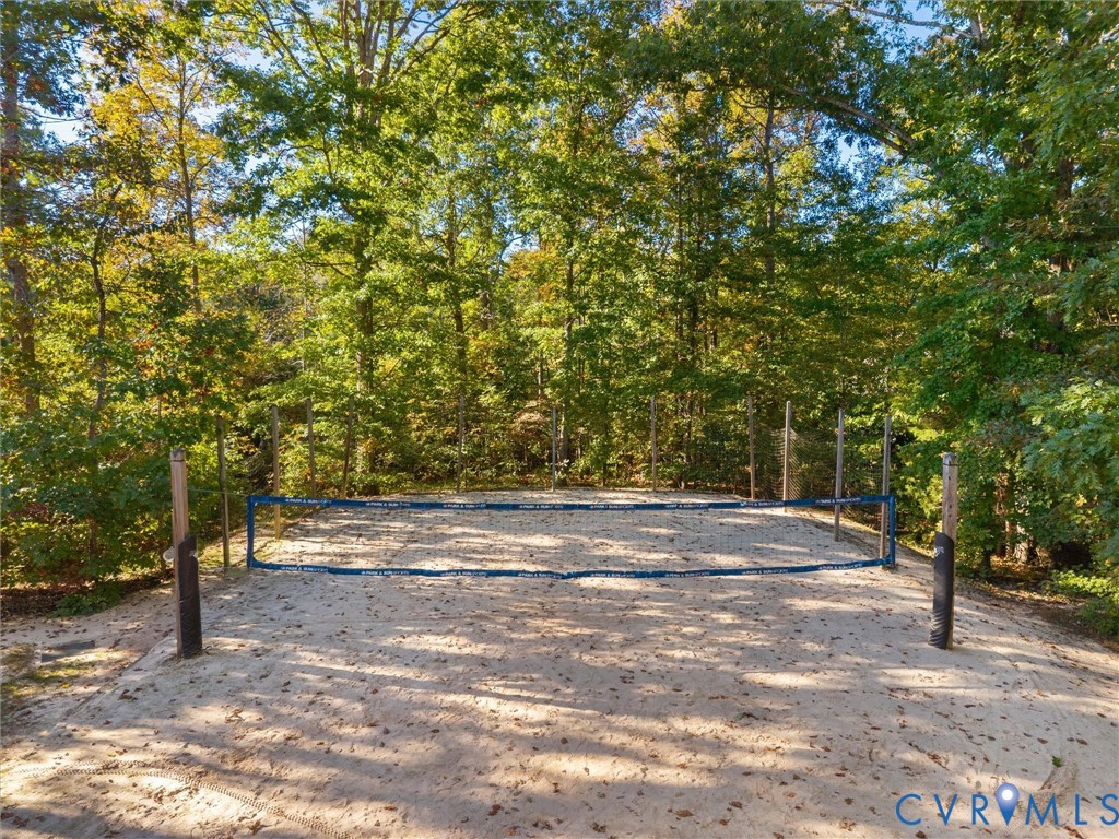Sand volleyball court featuring a permanent net system, vertical support posts, and perimeter fencing surrounded by mature trees