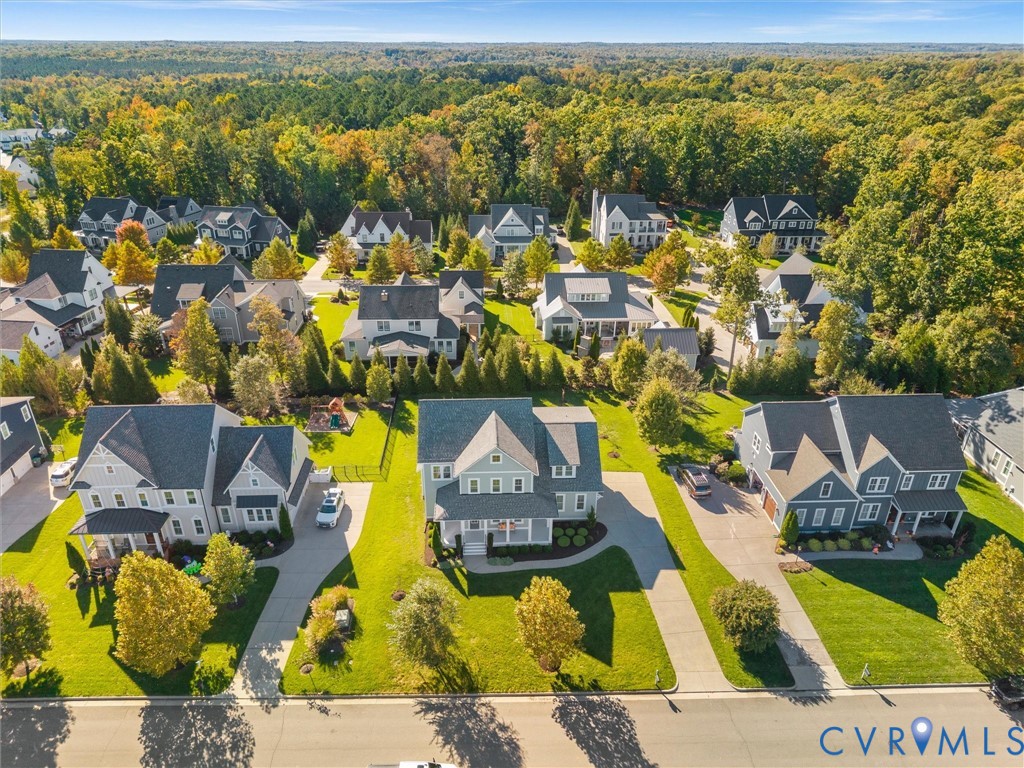 Aerial perspective of the residential community featuring multi-story dwellings, paved concrete driveways, manicured lawns, and mature landscaping