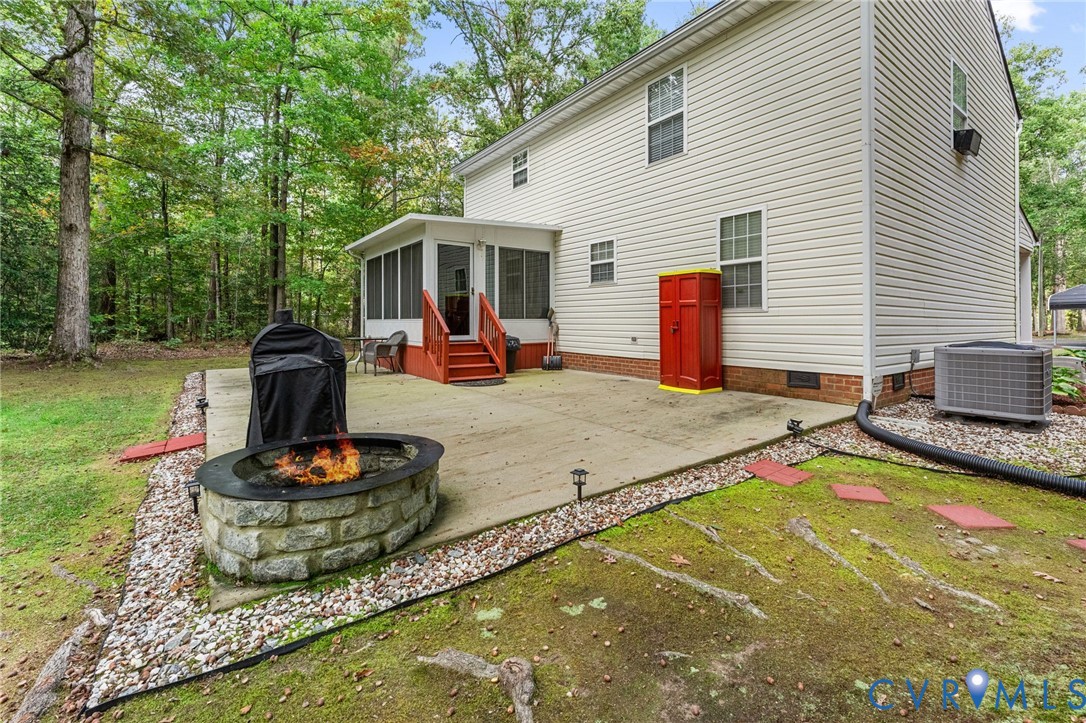 Concrete patio featuring a stone-faced fire pit, screened-in porch with painted wood stairs, and vinyl siding exterior