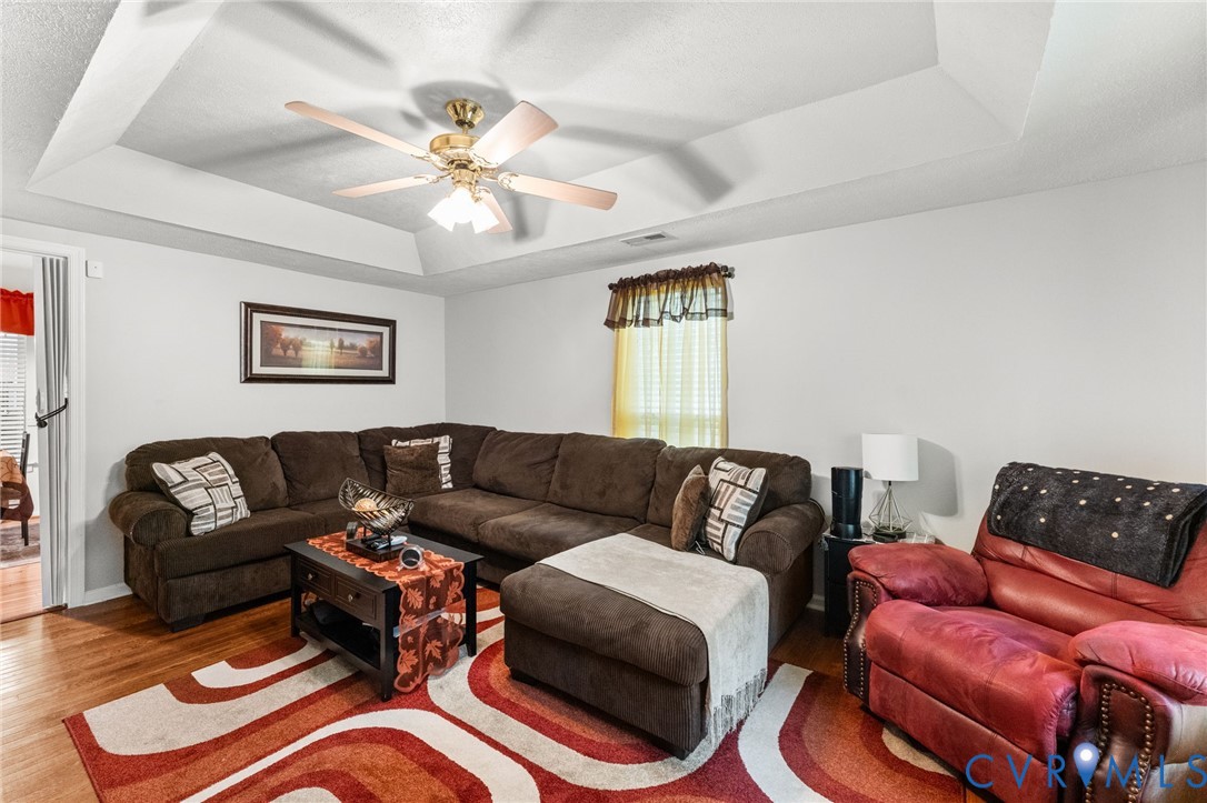 Tray ceiling, wood-finish flooring, and a central ceiling fan with integrated lighting