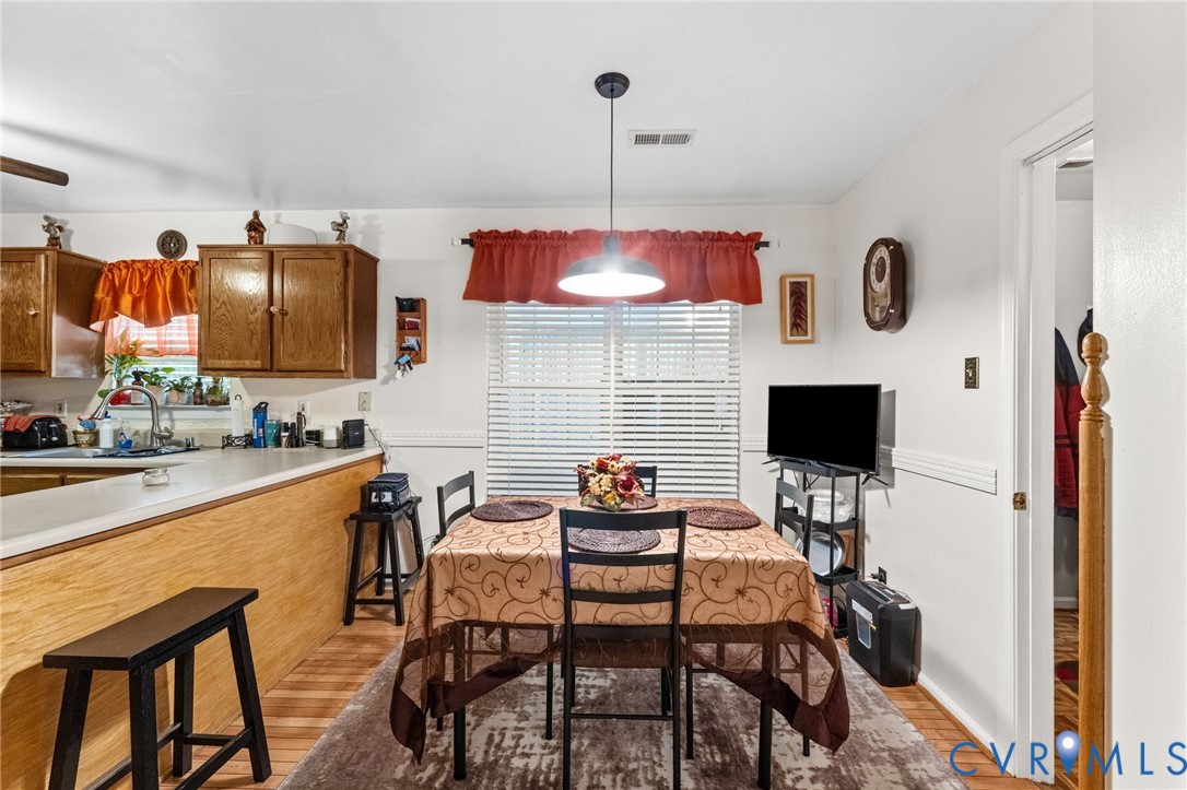 Kitchen featuring wooden cabinetry, a wrap-around peninsula, wood-finish flooring, chair rail molding, and a central pendant light fixture
