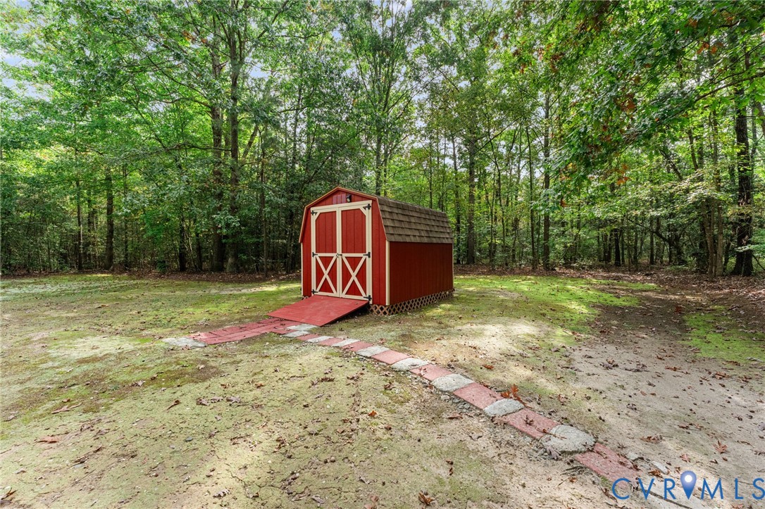 Gambrel-roof storage shed featuring double-door entry, a ramp, and a stone-paver walkway situated on a wooded lot