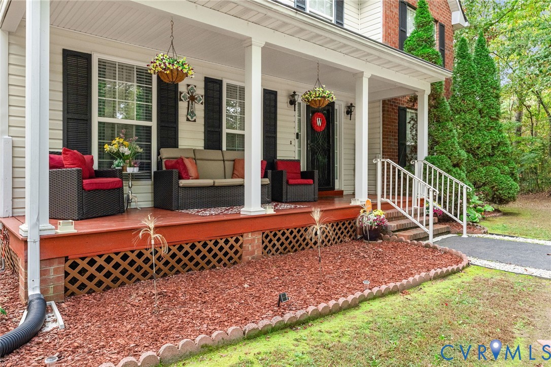 Covered front porch featuring a painted wood deck, lattice skirting, white support columns, and white metal railing