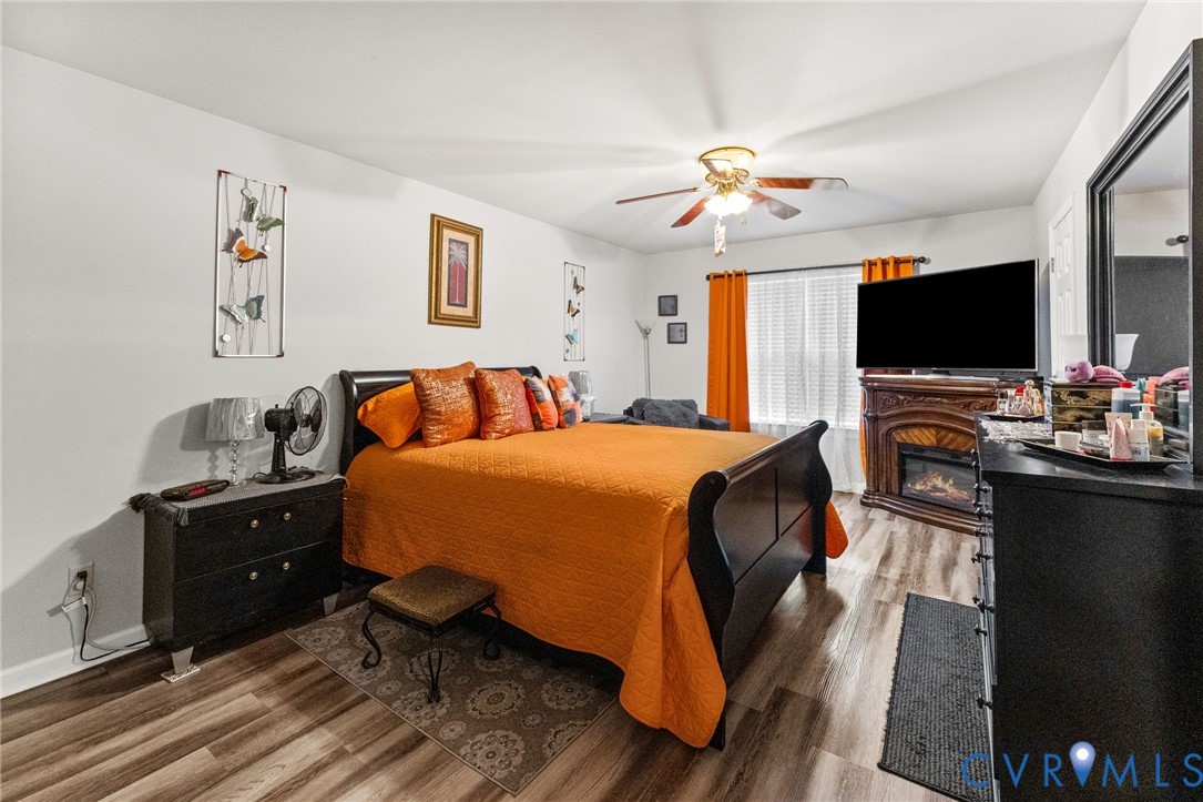 Wood-finish flooring, corner electric fireplace with ornate mantel, and a ceiling fan with integrated light fixture