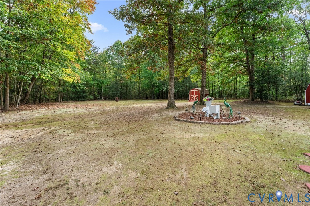 Expansive grounds featuring mature shade trees, a stone-bordered landscape bed, and a detached storage structure