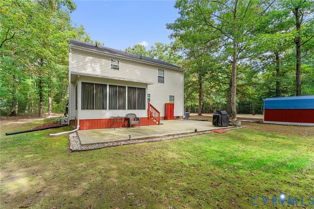 Rear exterior featuring a concrete patio, a screened-in porch with wood-finish siding, and a detached storage structure set against a wooded landscape