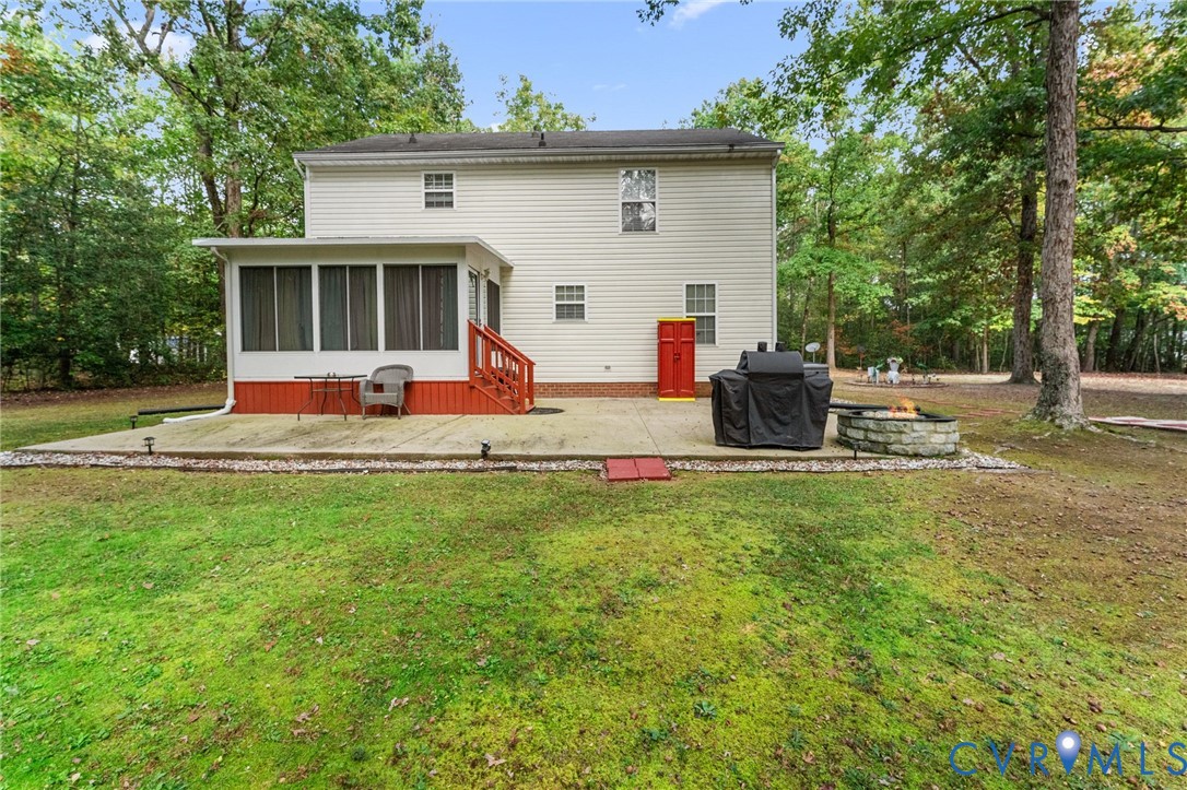 Rear exterior featuring light-toned vinyl siding, a screened-in porch with wood-style steps, a concrete patio, and a stone-encased fire pit