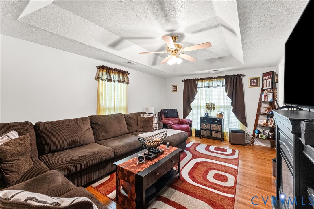 Living area featuring a tray ceiling, wood-finish flooring, and a multi-blade ceiling fan with integrated lighting