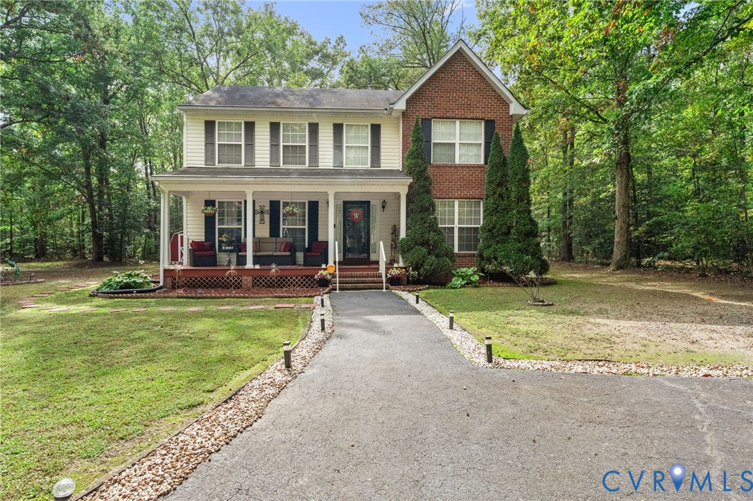 Two-story exterior featuring a brick and siding facade, expansive front porch with railing, and asphalt driveway