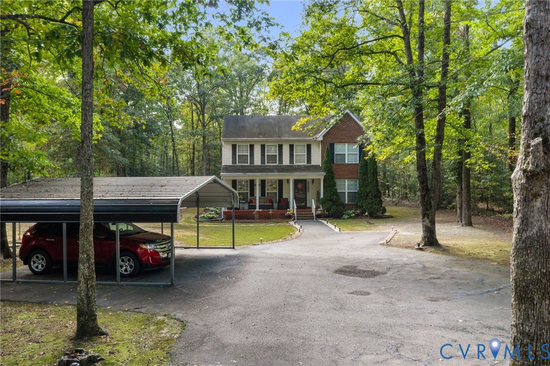 Two-story brick and siding colonial exterior featuring a front porch, an asphalt driveway, and a detached metal carport