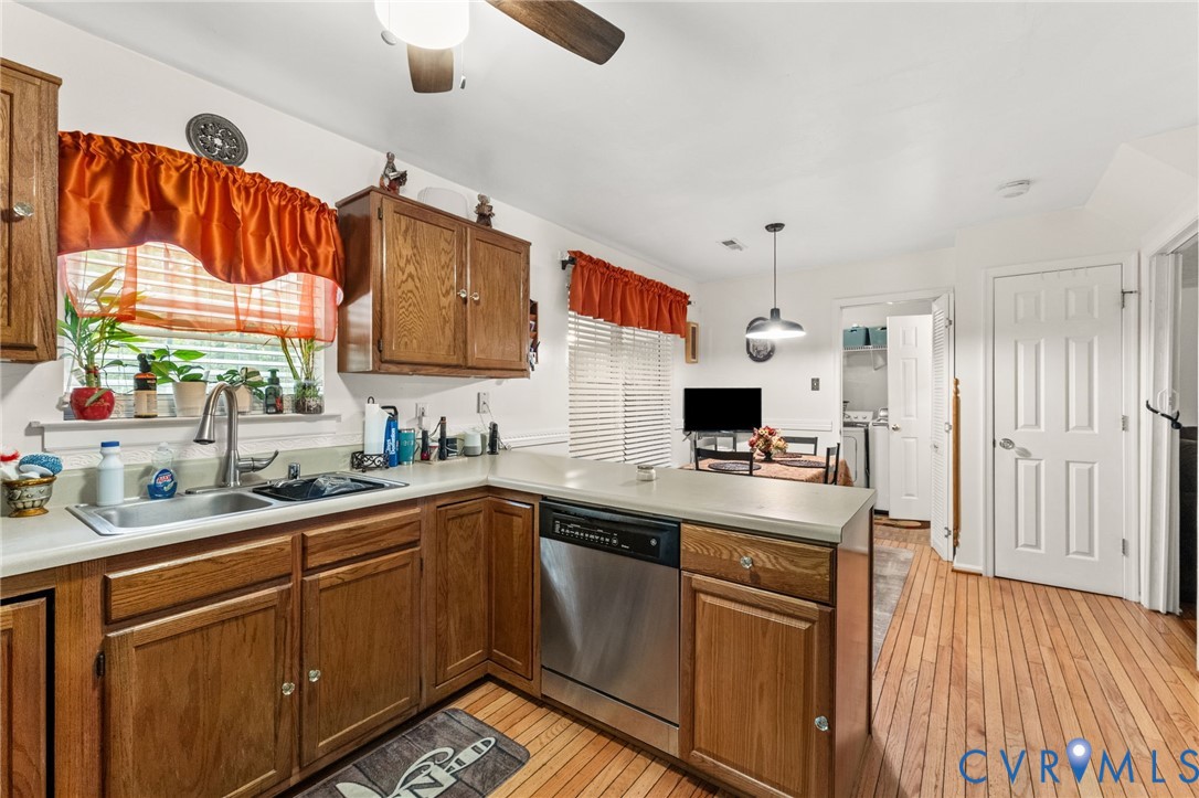 Kitchen featuring wood cabinetry, stainless steel dishwasher, wood-finish flooring, dual-basin stainless steel sink, and ceiling-mounted pendant lighting