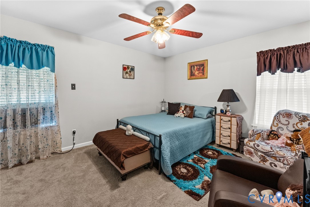 Neutral wall coloring, wall-to-wall carpeting, and a ceiling-mounted light fixture with a multi-blade fan
